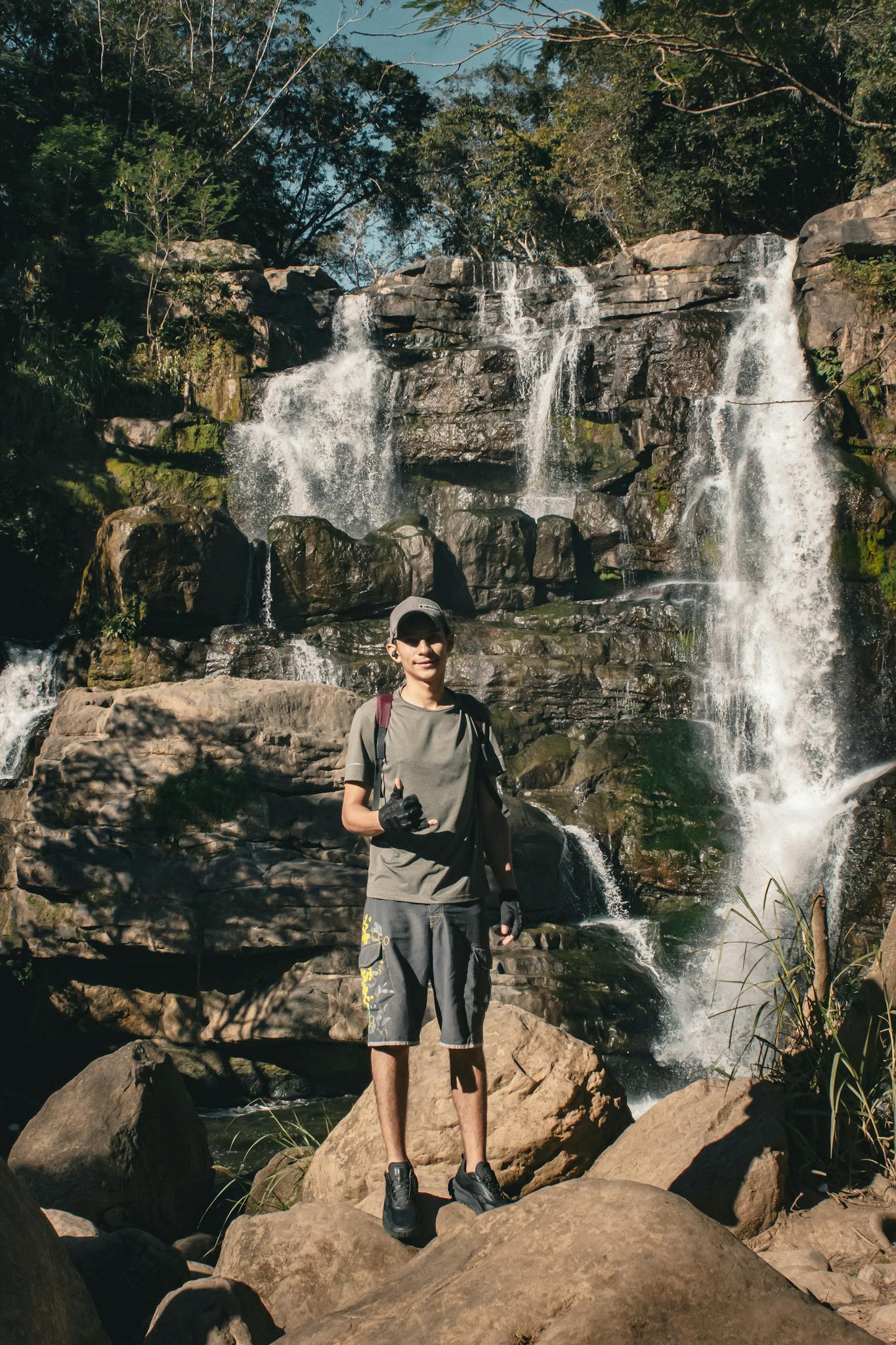 A young hiker stands confidently in front of a cascading waterfall, capturing the essence of outdoor adventure.